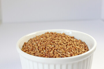 White bowl is filled with raw buckwheat groats, ready for cooking and serving