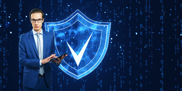 Businessman in suit using a tablet with a shield checkmark hologram in the background, representing cyber security concept.