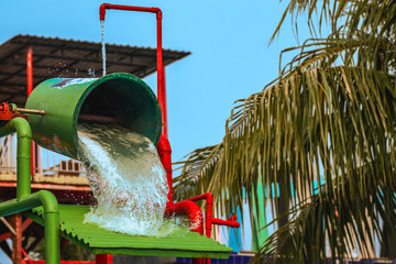Water spills on the water bucket attraction in water park. Water splash on tipping bucket or water bucket in swimming pool. Water park and swimming pool rides. Freezing photo water splash.