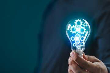 Hand holding light bulb with glowing gears symbolizing ideas, innovation, and technology. Blue...