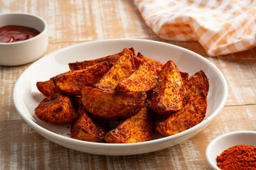 Air Fryer Roast Potatoes on a plate,potato wedges with paprika flavor and tomatoes sauce on table.