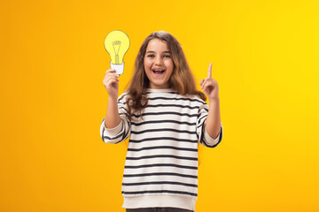 Surprised child girl holding paper bulb and pointing finger up. Success, motivation, winner, genius, idea concept