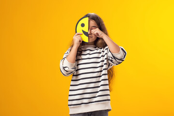 Crying Kid girl holding half face happy emoticons in front of her face. Mental health, psychology and children's emotions concept