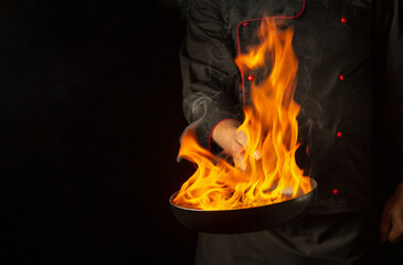 A chef cooking food on frying pan with fire flame or flambe. Concept of cooking food for lunch in...