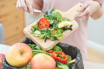 Compost from leftover food, asian young housekeeper woman hand holding cutting board use fork scraping waste, rotten vegetable throwing away into garbage, trash or bin. Environmentally responsible.