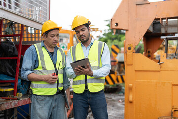 Two construction crane workers in safety vests and helmets using a tablet for planning and...