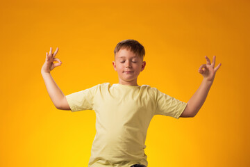 Kid boy smiling peacefully holding his fingers in mudra gesture, meditating. Zen, meditation,...