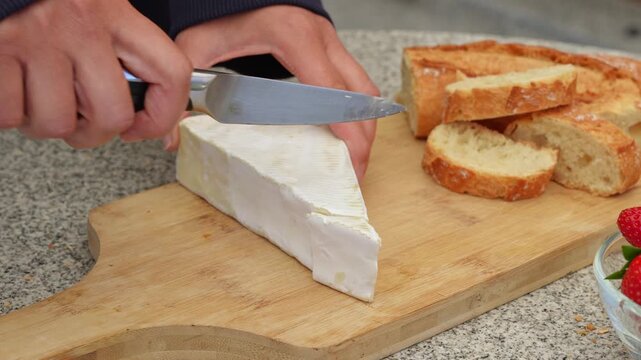 Women's hands prepare sliced brie cheese and serve it with a French baguette, aperitif on the French-style terrace
