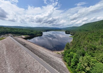 Aerial view of dam and reservoir in New England surrounded by lush green forest mountains. Drone photo of Surry Mountain Lake in Surry, New Hampshire.