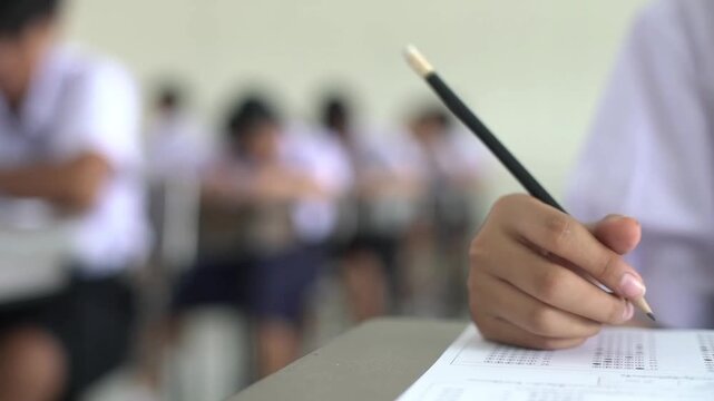 Close up hand of student reading and writing exam answer sheets exercises with stress in classroom