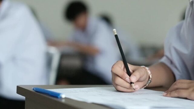 Close up hand of student reading and writing exam answer sheets exercises with stress in classroom