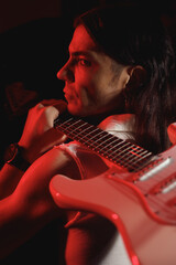 Guitarist portrait illuminated with red light, holding guitar on shoulder..