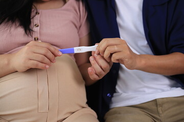 Happy man with pregnant wife rubbing his belly while relaxing and spending time in modern apartment. Pregnant woman and husband spending time together using smartphone