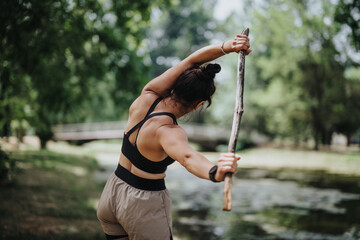 Woman stretching and exercising with a wooden stick in a park, promoting fitness and peaceful...