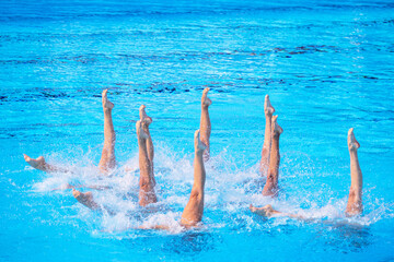 Synchronized female artistic swimming team performing synchronized legs movement in swimming pool