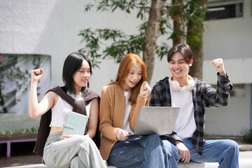 Three young people are looking at a laptop and raising their fists in the air, happy about their accomplishments