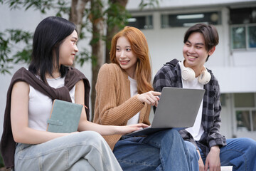 Three students happily collaborating on a project outdoors, using a laptop on campus. Friends engaged in discussion outside a modern building, showcasing teamwork and technology in education