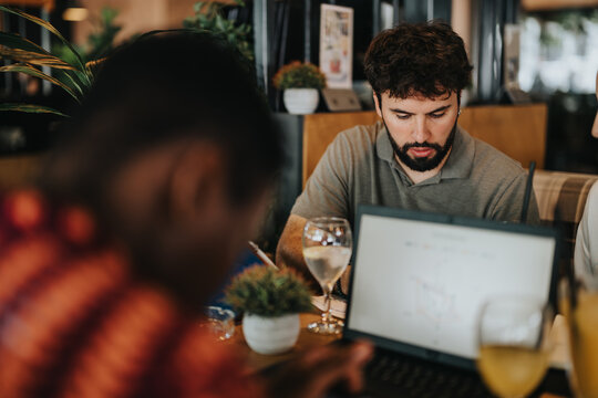 Diverse group of people engaging in a collaborative meeting at a cozy coffee bar, focusing on a laptop and discussing ideas.