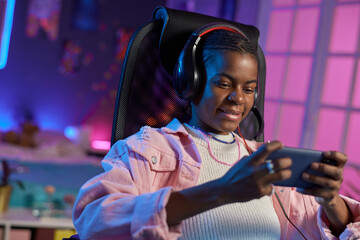 Portrait of teenage African American girl playing mobile games while relaxing at home at night © Mediaphotos