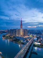 Landmark building illuminated night drone shot with Saigon river boat traffic and road traffic on the bridge below in vertical format. A dynamic welcome establishing Ho Chi Minh City, Vietnam.