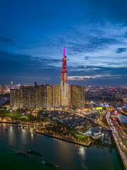 Landmark building illuminated night drone shot with Saigon river boat traffic and road traffic on the bridge below in vertical format. A dramatic welcome to Ho Chi Minh City, Vietnam.