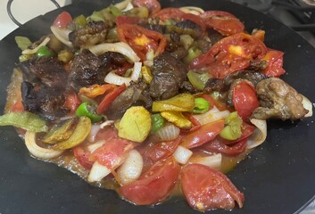 a mixture of chopped meat, tomatoes, onions, peppers, potatoes, and eggplant is cooked in a pan of oil