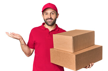 Hispanic male courier with boxes showing a copy space on a palm and holding another hand on waist.