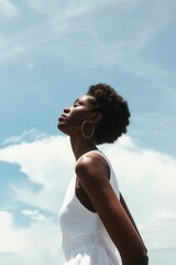 Obraz premium A woman in a white dress gazes upward against a bright blue sky, embodying freedom and hope in her expression.
