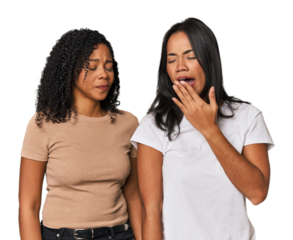 Young Latin friends in studio yawning showing a tired gesture covering mouth with hand.