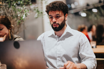 Young man intensely focused on his laptop screen while sitting in a modern cafe. Casual setting, thoughtful expressions, and a blurred background add depth to the image.