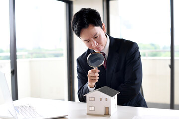 虫眼鏡で住宅模型を覗くスーツ姿の若い男性