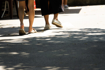 Two women walking on a sidewalk. One is wearing sandals and the other is wearing flats