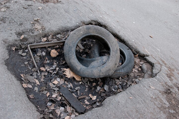 Old torn tires lie in a hole in the asphalt road, with the remnants of a storm drain at the bottom...