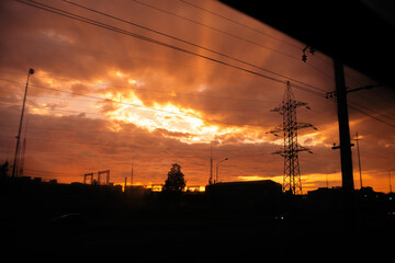 Fototapeta premium The view from the train window at sunset, with the power line and silhouetted city houses. The journey is taking place in the evening.