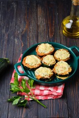 Zucchini stuffed with minced chicken and baked with cheese and herbs in a green baking dish on a dark wooden background.