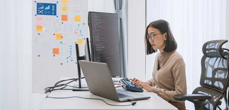 Young adult Asian female software developer coding program on desktop computer. Woman work from home, remote working, freelance programmer job, smart digital nomad lifestyle concept