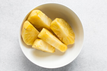 Top view of peeled chopped pineapples in a white ceramic bowl, overhead view of chopped pineapples on a white background