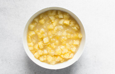 Overhead view of diced pineapple and sugar being mixed together in a white bowl, process of making pineapple cheong or pineapple syrup