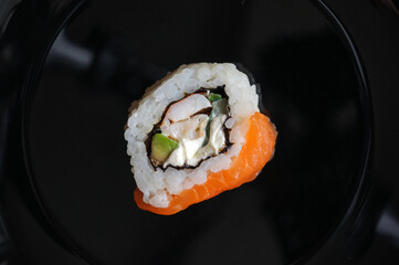 Top view of one sushi roll on black plate with cream cheese cucumber and avocado. Close-up. Space for text