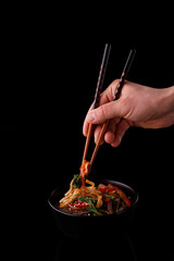 Stir fry noodles with vegetables and shrimps in black bowl. Slate background. Top view. Copy space.