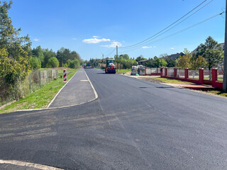 Fototapeta premium Laying the last layer of asphalt on the modernized road and sidewalk. Operation of a machine for laying asphalt and road rollers