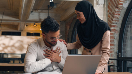 Male Arabian man businessman intern studying working laptop computer at office Muslim woman female businesswoman in hijab boss business leader mentor help check approve good job praise happy employee