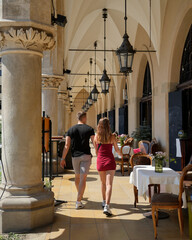 A couple enjoys a leisurely stroll in a summer street restaurant featuring elegant medieval arches and cozy tables. This charming scene captures the essence of romantic dining and historic ambiance