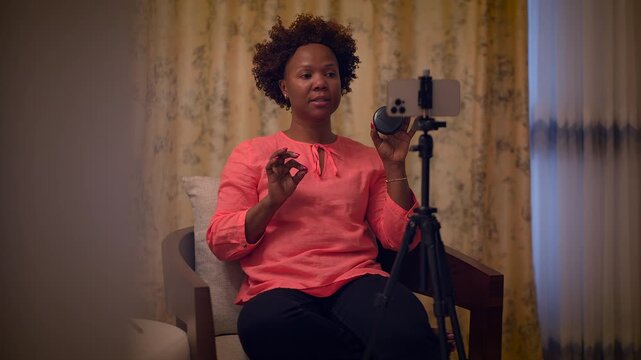 In her home studio, a woman is happily using a smartphone mounted on a tripod to film a video
