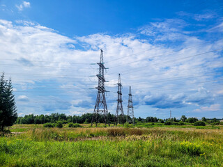 Torres de alta tensión sobre un campo verde bajo un cielo azul con nubes dispersas.