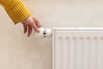 Man or woman in warm clothes turns the battery heating knob. Gas or electric heating in home