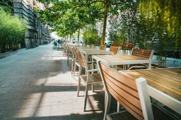 Street restaurants tables. Sidewalk among urban greenery.