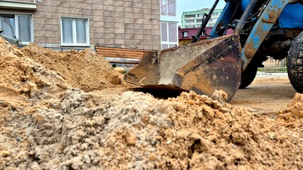 Fototapeta premium Construction Equipment Moves Sand at Residential Site During Daytime Near Urban Area