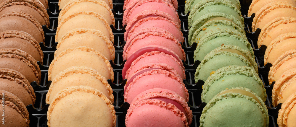 Poster multi-colored macarons in a plastic box, top view.