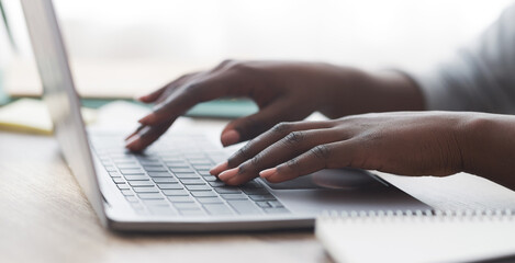 Fototapeta premium Closeup of unrecognizable afro woman typing on laptop keyboard while working in office, panorama